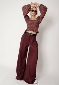 Maroonowy top w kwiatowy wzór z marszczeniami, połączony z szerokimi, granatowymi spodniami. Modelka nosi okulary przeciwsłoneczne i czarny pasek.