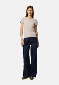 Beige ribbet kortærmet T-shirt parret med høj talje, bredbenede mørke denim jeans. Modellen bærer brune casual sko.