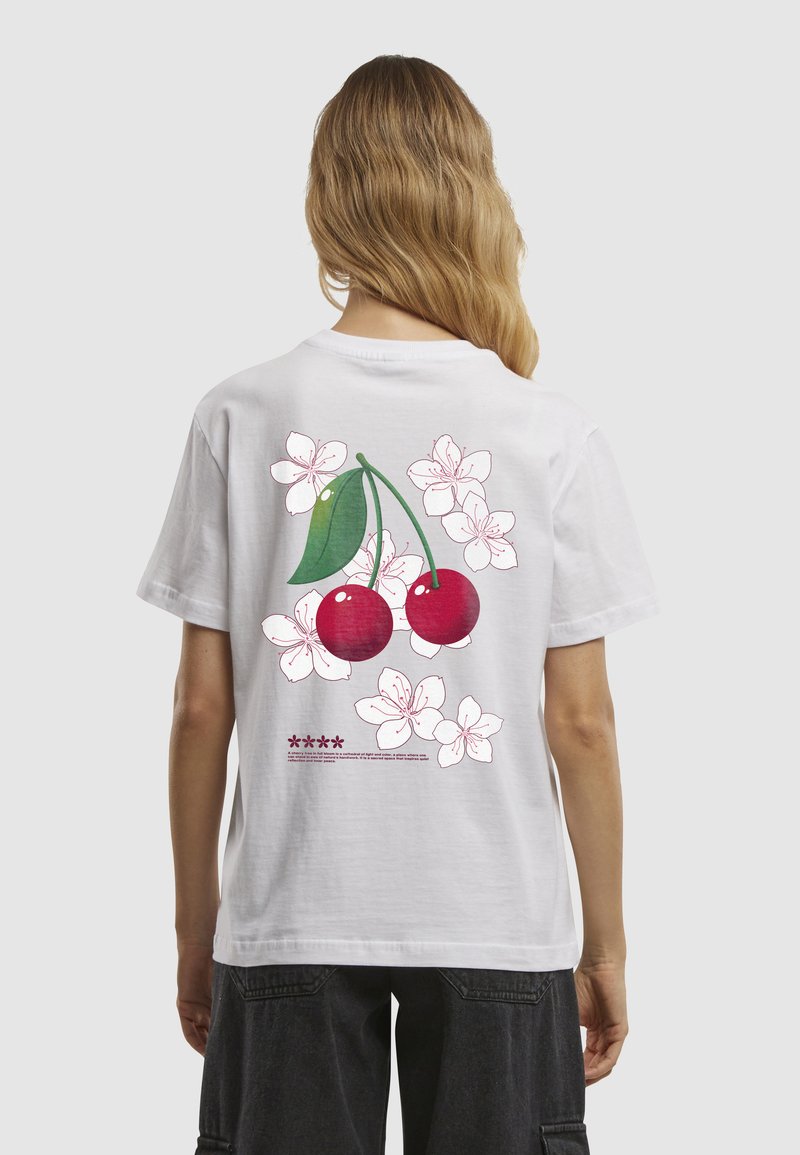 T-shirt en coton blanc avec un graphique de deux cerises rouges et des fleurs roses au dos, avec un texte détaillé sous le dessin.