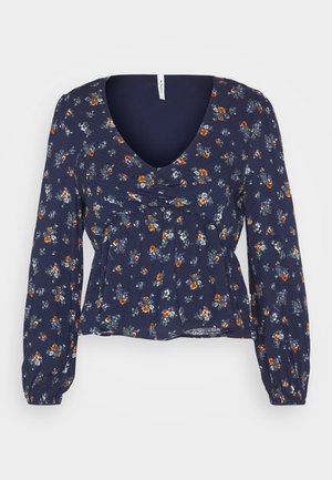 Blusa floral azul marino con largas mangas abullonadas, escote en V profundo y cintura fruncida. Presenta pequeñas flores en naranja, blanco y azul sobre un tejido texturizado.