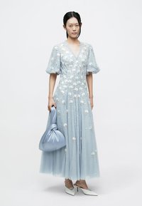 Ljusblå klänning med blommig brodyr, puffärmar och ett flödande kjol, kombinerad med en mjuk blå handväska och vita spetsiga pumps.