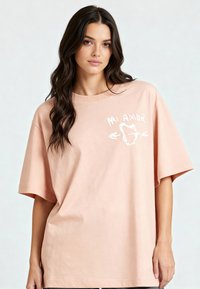 T-shirt en coton surdimensionné rose avec le texte imprimé en blanc "Mi Amor" et un design de cœur avec des flèches, à manches courtes et à coupe décontractée.