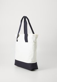 Tote bag van witte stof met een marineblauwe bodem. Heeft dubbele marineblauwe handvatten en een minimalistisch ontwerp met een gestructureerde vorm.