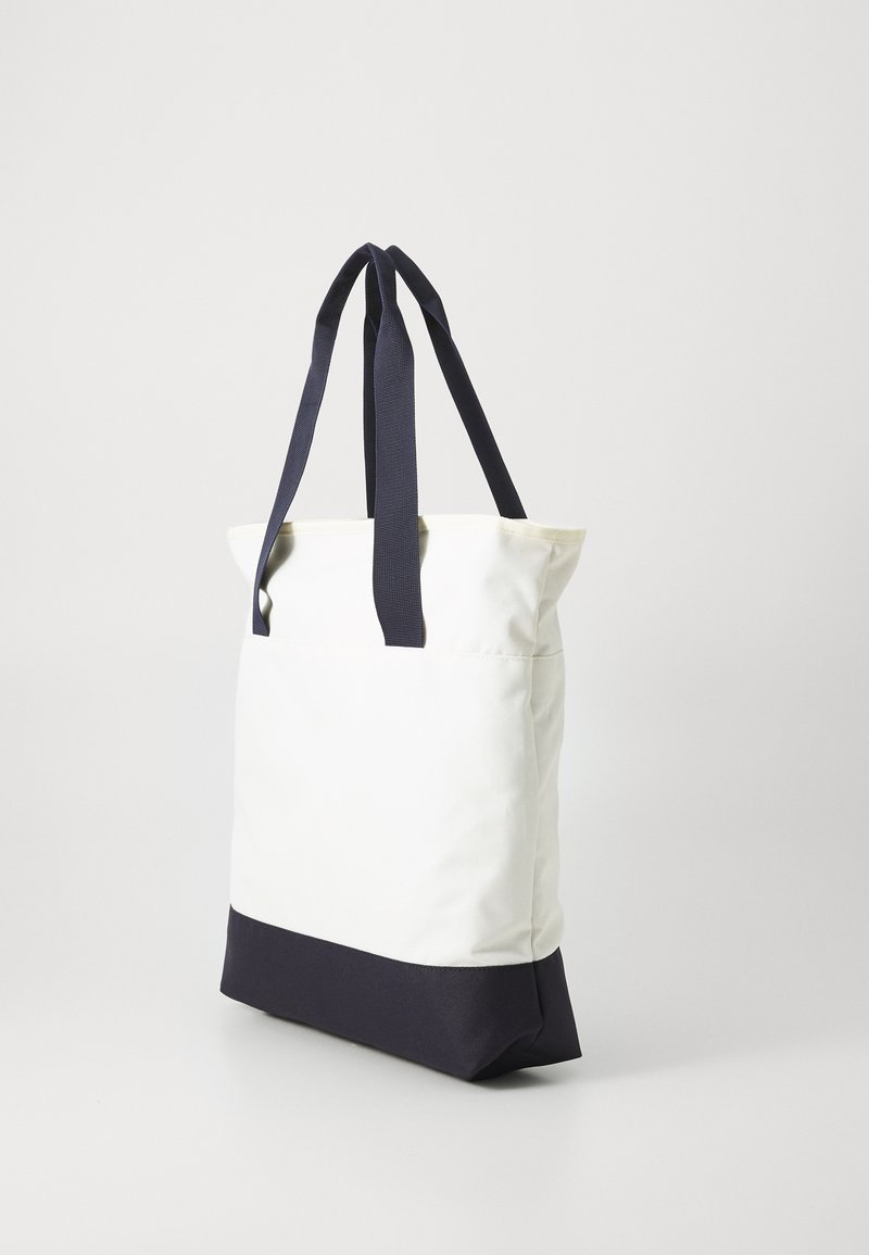 Borsa a spalla in tessuto bianco con fondo blu navy. Presenta doppi manici blu navy e un design minimalista con una forma strutturata.