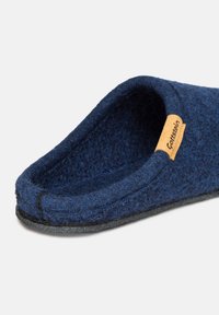 Pantofole in feltro di lana blu con suola nera e un piccolo etichetta beige che recita "Gottstein" sul lato vicino all'apertura.