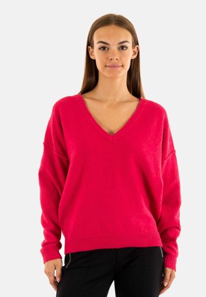 Suéter de gran tamaño en fucsia con escote en V, dobladillo acanalado y mangas largas. Textura suave y ajuste relajado, combinado con pantalones oscuros.