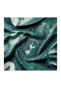 Giacca sportiva verde e testurizzata con un logo al centro, con un collo rotondo e dettagli in tessuto decorativi in tutto il capo.