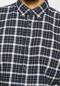 Navy and white checkered shirt. Button-down collar, short sleeves, plaid pattern, fabric appears soft with a textured finish.