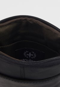 Interno di una borsa in pelle nera con apertura con zip. Presenta una fodera in tessuto scuro e un'etichetta con un logo. Texture liscia e forma arrotondata.