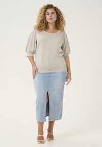 Lichtbeige gebreide trui met korte pofmouwen, gecombineerd met een lichtblauwe denim kokerrok met een split aan de voorkant. Huidskleurige sandalen maken de look compleet.