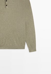 Licht olijfgroene gebreide trui met lange mouwen, drie zwarte knopen op de bovenborst en geribbelde boorden en zoom.