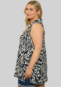 Ärmellose Bluse in marineblau und creme mit einem wirbelnden Muster. Verfügt über eine lockere Passform, seitliche Schlitze und einen Kragen. Weicher Stoff.