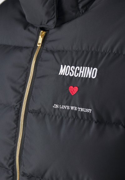 Padded crna jakna s visokim ovratnikom, zlatnim zatvaračem, bijelim 'MOSCHINO' logotipom, crvenim srcem i izvezenim tekstom 'U LJUBAVI VJERUJEMO' na prednjem dijelu.