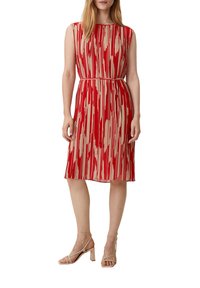Rotes und beige gemustertes Kleid mit kurzen Ärmeln, tailliertem Schnitt und knielangem Rock; mittlere Textur und glattes Material; kombiniert mit beigen Sandalen.
