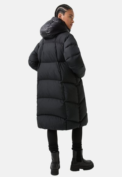 Puffy black coat with a shiny hood, featuring horizontal stitching and a knee-length design. Worn with black leggings and chunky boots.