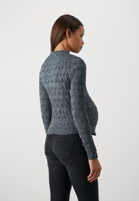 Tmavo šedý textured top s dlhým rukávom a kvetinovým vzorom, priliehavého strihu a okrúhlym výstrihom, skombinovaný s čiernymi džínsami.