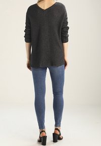 Maglione grigio a maglia con scollo a V, maniche arrotolate e un retro leggermente più lungo. Abbinato a jeans skinny blu e sandali neri con tacco.