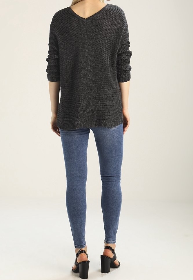 Maglione grigio a maglia con scollo a V, maniche arrotolate e un retro leggermente più lungo. Abbinato a jeans skinny blu e sandali neri con tacco.