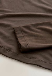 Bruine katoenen T-shirt met een gladde textuur. Heeft een opgevouwen mouw en zichtbare stiksels langs de zoom en de rand van de mouw.