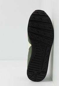 Green athletic shoe with a textured black rubber sole, featuring a distinct tread pattern and cream-colored accents on the side.
