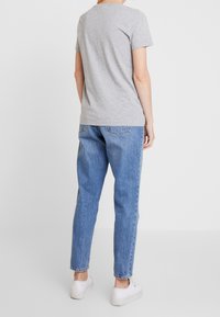 Camisa de algodón gris con mangas cortas, combinada con jeans de mezclilla azul claro. Los jeans tienen bolsillos traseros y un diseño de pierna ajustada.