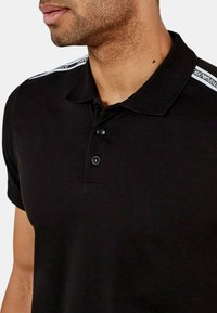 Polo shirt nera in cotone con tre bottoni, dotata di accenti bianchi sulle spalle e un design del colletto classico.