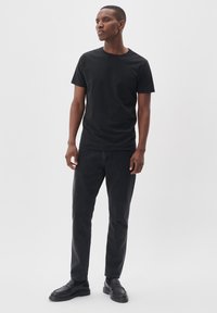 Tricou din bumbac negru cu guler rotund, combinat cu jeansi închiși la culoare și mocasini negri. Întreaga ținută are un design simplu și casual.