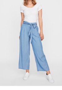 Ljusblå vida byxor med ett knytbälte i midjan, gjorda av denimtyg. Kombinerat med en åtsittande vit t-shirt och vita sneakers.