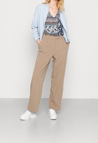 Veste bleu clair, haut à motifs bleu marine et blanc, pantalon à jambes larges beige et baskets blanches épaisses, présentant des tissus lisses et des lignes épurées.