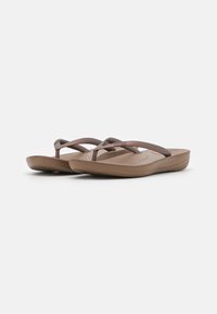 Brune flip-flops med kryssbånd, laget av teksturert gummi. Har en polstret såle og en liten hæl for komfort.