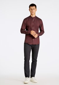 Bordeaux overhemd met knoopsluiting en hoge kraag, slim fit, en lange mouwen. Gecombineerd met zwarte slim-fit broek en witte sneakers.
