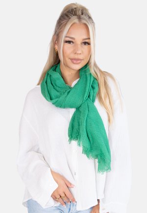Green textured scarf with frayed edges, worn around the neck, paired with a white button-up shirt.