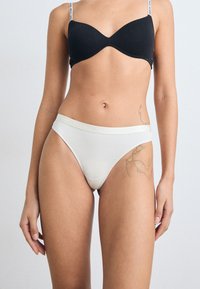 White cotton thong with a soft waistband, featuring a logo detail. Smooth texture, minimalist design, and side coverage.