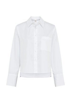 Hvid langærmet skjorte med knapper, spids krave, brystlomme foran og brede manchetter på ærmerne.