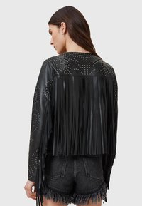 Juoda odinė striukė su kutais ir kniedėmis ant nugaros. Trumpas, aptemptas stilius su lygiu paviršiumi.