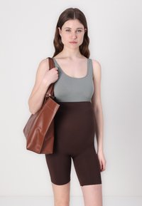 Brown high-waisted shorts with a smooth texture paired with a light green sleeveless top. The model holds a brown leather tote bag.