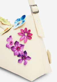 Cremefarbene Handtasche mit strukturierter Oberfläche, verziert mit bunten Blumenapplikationen in Blau, Gelb, Pink und Lila. Verstellbare Trägerdetails.