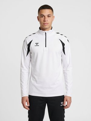 Ung mand iført en hvid langærmet sportstop med sorte accenter og matchende sorte bukser med et logo fra et sportsmærke.