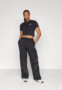 Schwarzes Cropped-T-Shirt mit rundem Logo und schwarzen Sporthosen, die pinke und weiße geschwungene Akzente aufweisen und aus leichtem Stoff gefertigt sind.