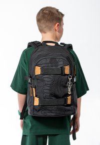 Zaino in tessuto nero con design testurizzato, dettagli arancioni, spallacci regolabili e un portachiavi attaccato. Adatto per trasportare libri e materiali.