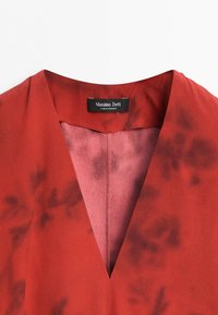 Red garment with a V-neck collar and subtle dark floral patterns, featuring a black label that reads Massimo Dutti made in Morocco.