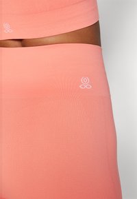Høyt liv, tettsittende tights i ferskenfarget stoff. Har ribbestruktur og en liten hvit logo på livkanten, glatt finish.