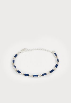 Sudraba rokassprādze ar taisnstūra tumši ziliem akmeņiem, kas savienoti ar nelielām sudraba cilpām un regulējamu ķēdes aizdari uz balta fona.