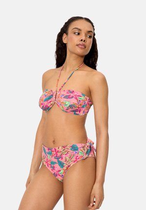 Mujer con un bikini de dos piezas rosa con estampado floral y tirantes halter, mirando hacia un lado contra un fondo liso y claro.