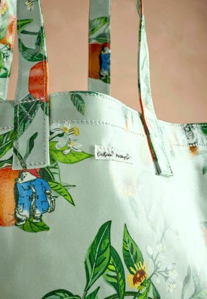 Hele rohelise tooni kandekott, millel on lillemustrid, erksate oranžide ja kollaste lilledega, roheliste lehtede ja küljele õmmeldud sildiga.