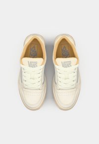 Vans-sneakers med en kremfarget beige læroverdel, perforert tå, lys grå aksenter og flate lisser. Glatt tekstur og polstret innvendig.