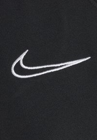 Svart tyg med en texturerad yta som har en vit broderad Nike Swoosh-logotyp, placerad något till höger.