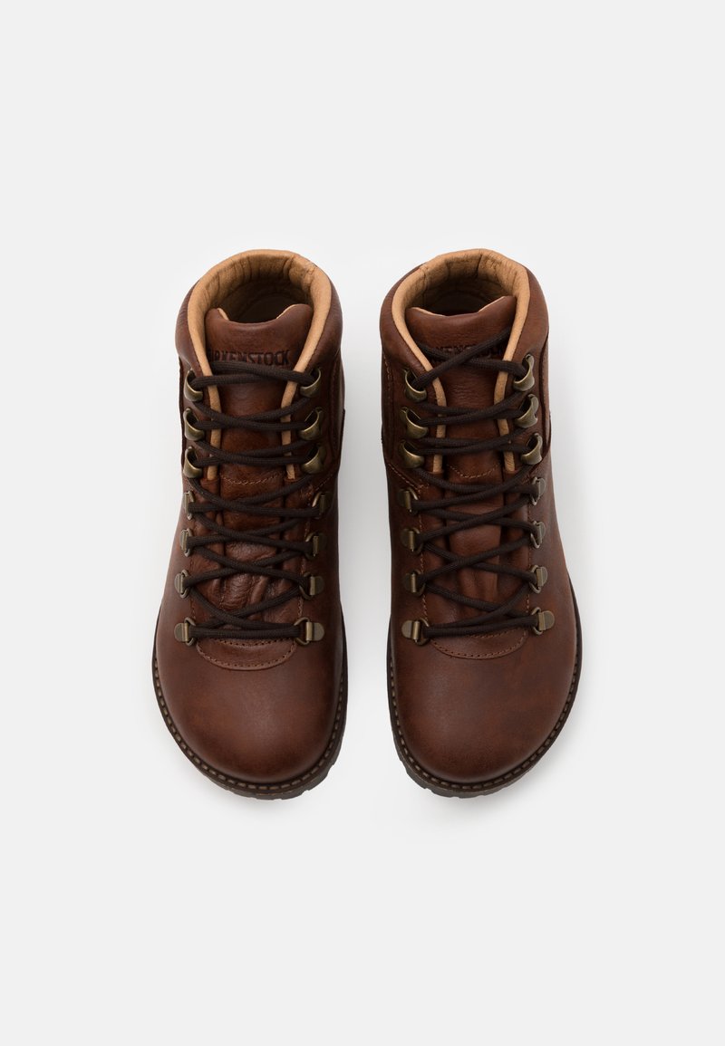 Ein Paar braune Lederwanderschuhe mit dunklen Schnürsenkeln und gepolsterten Kragen, von oben auf einem neutralen Hintergrund betrachtet.