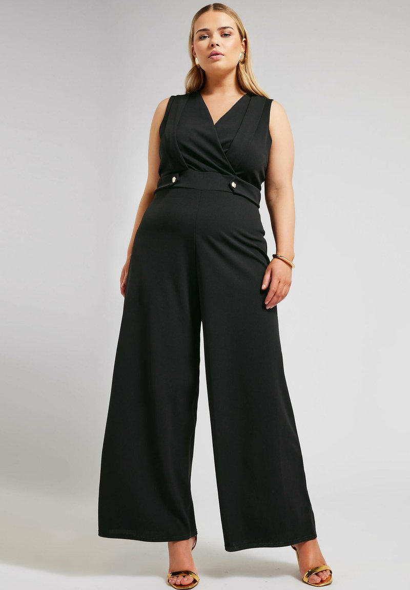 Svart jumpsuit med omslagsstil, ärmlös design och vida ben. Har en figurnära midja med knappdetaljer. Slät tygtextur.