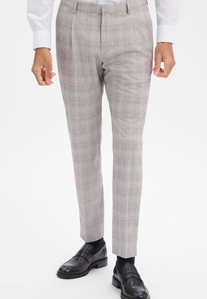 Herrenhose, hellgrau, schmal geschnitten, kariert, kombiniert mit schwarzen Socken und schwarzen Leder-Loafers, dazu sichtbar weiße Hemdärmel.